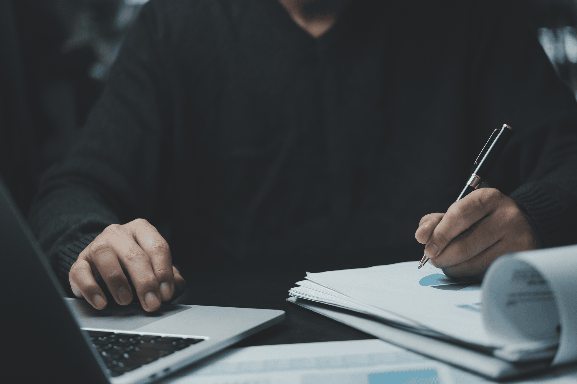 man writing on paper next to the laptop