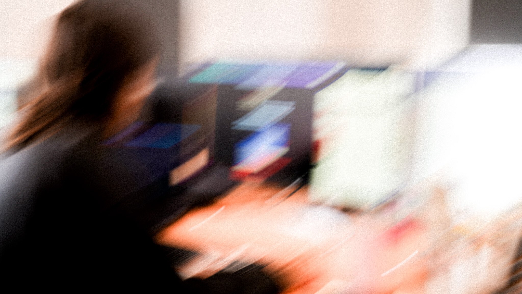 Blurred motion shot of someone at a desk, with computer monitors visible but out of focus in the background.