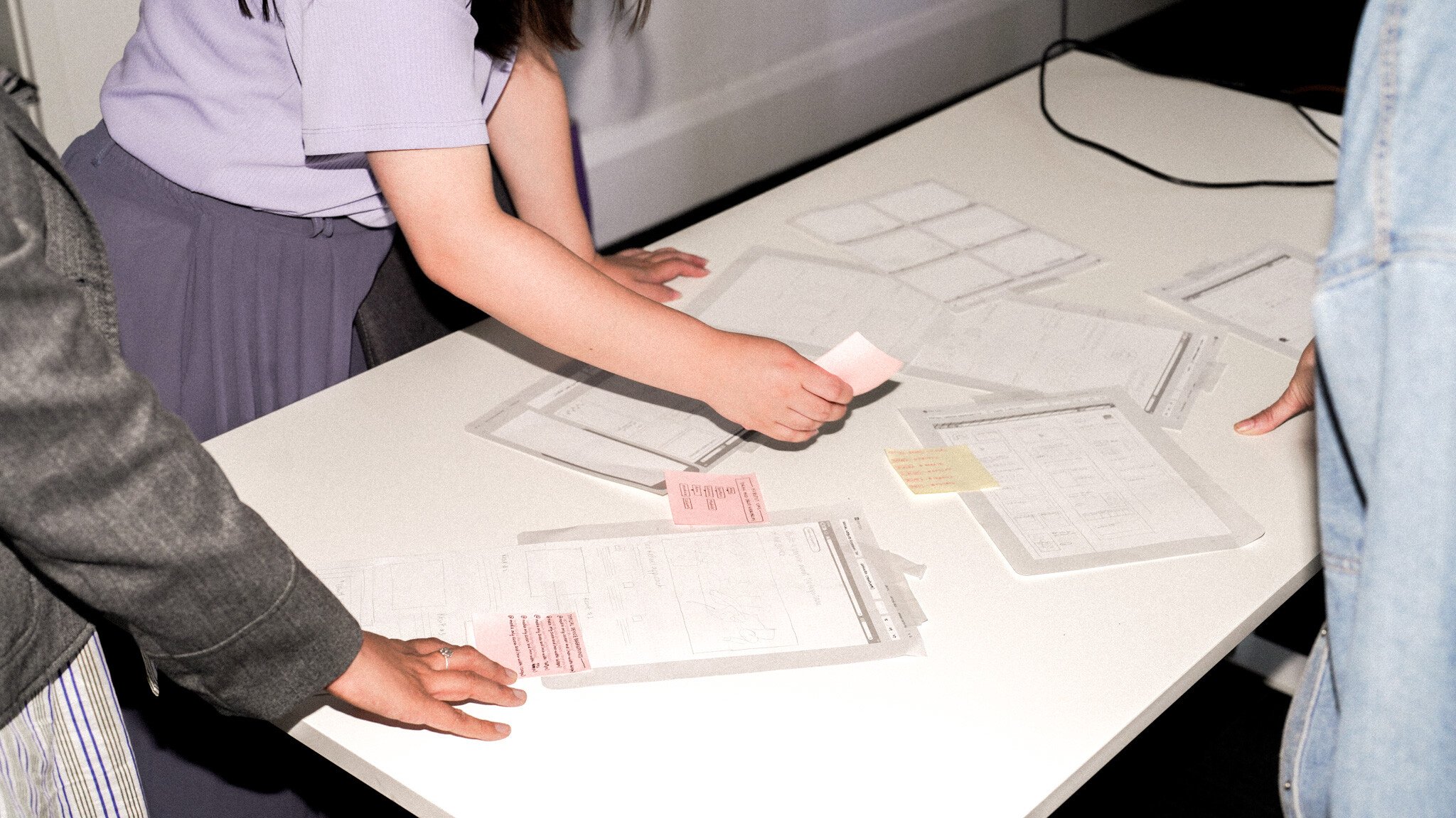 Hands arranging papers and sticky notes on a white table surface, showing a planning session in progress.