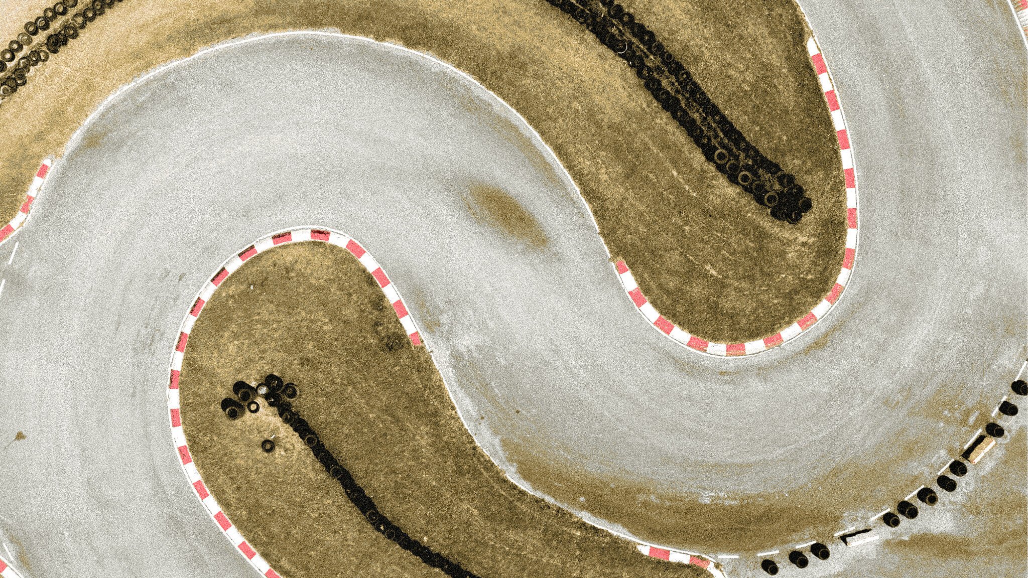 Aerial view of a go-kart race track section showing curved turns with red and white track borders, tire marks visible on the concrete surface, and rubber tire barriers along the edges.