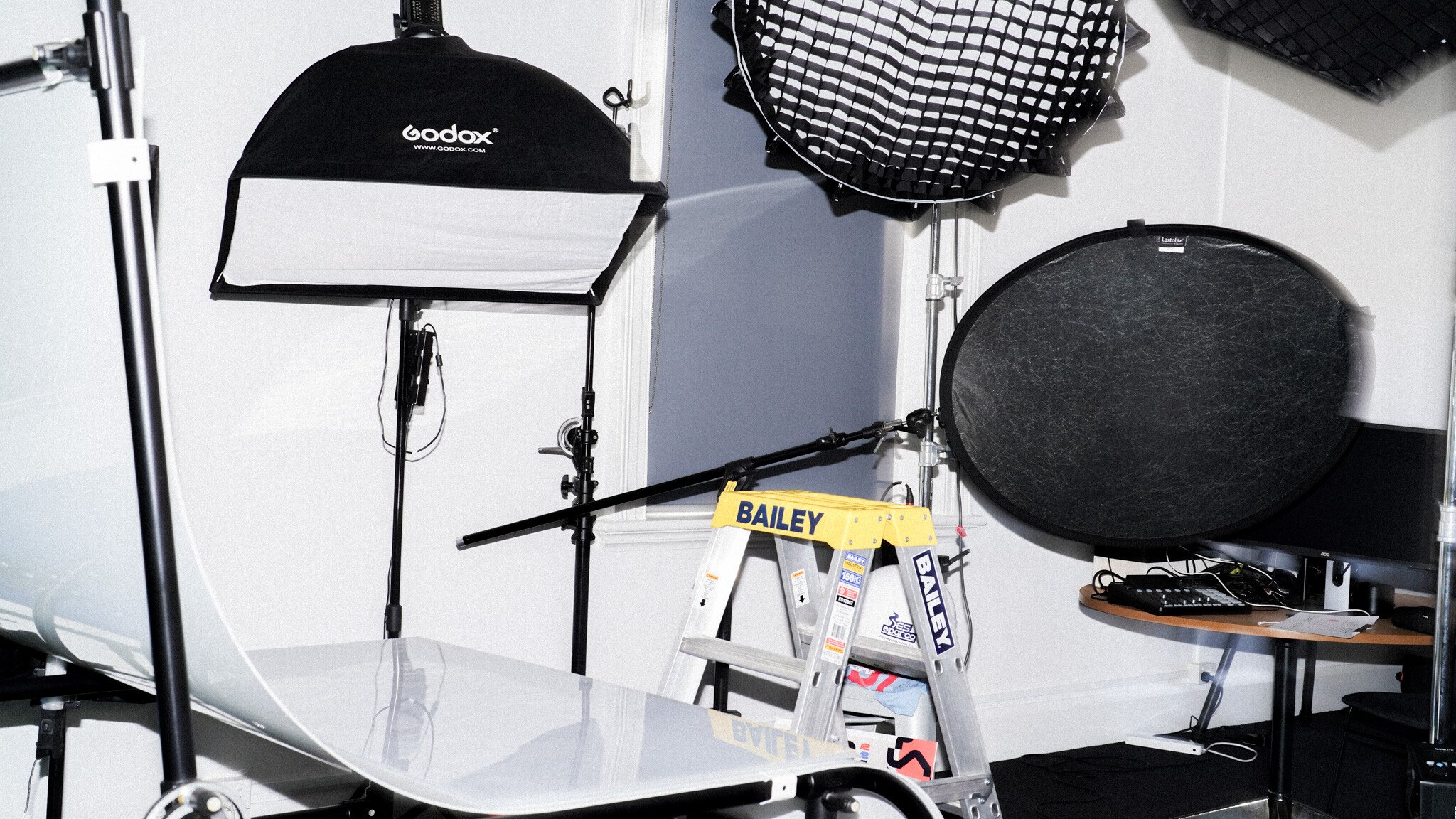 Photography and video studio setup showing lighting equipment, light modifiers including a softbox and grid, and a small step ladder against a white background.