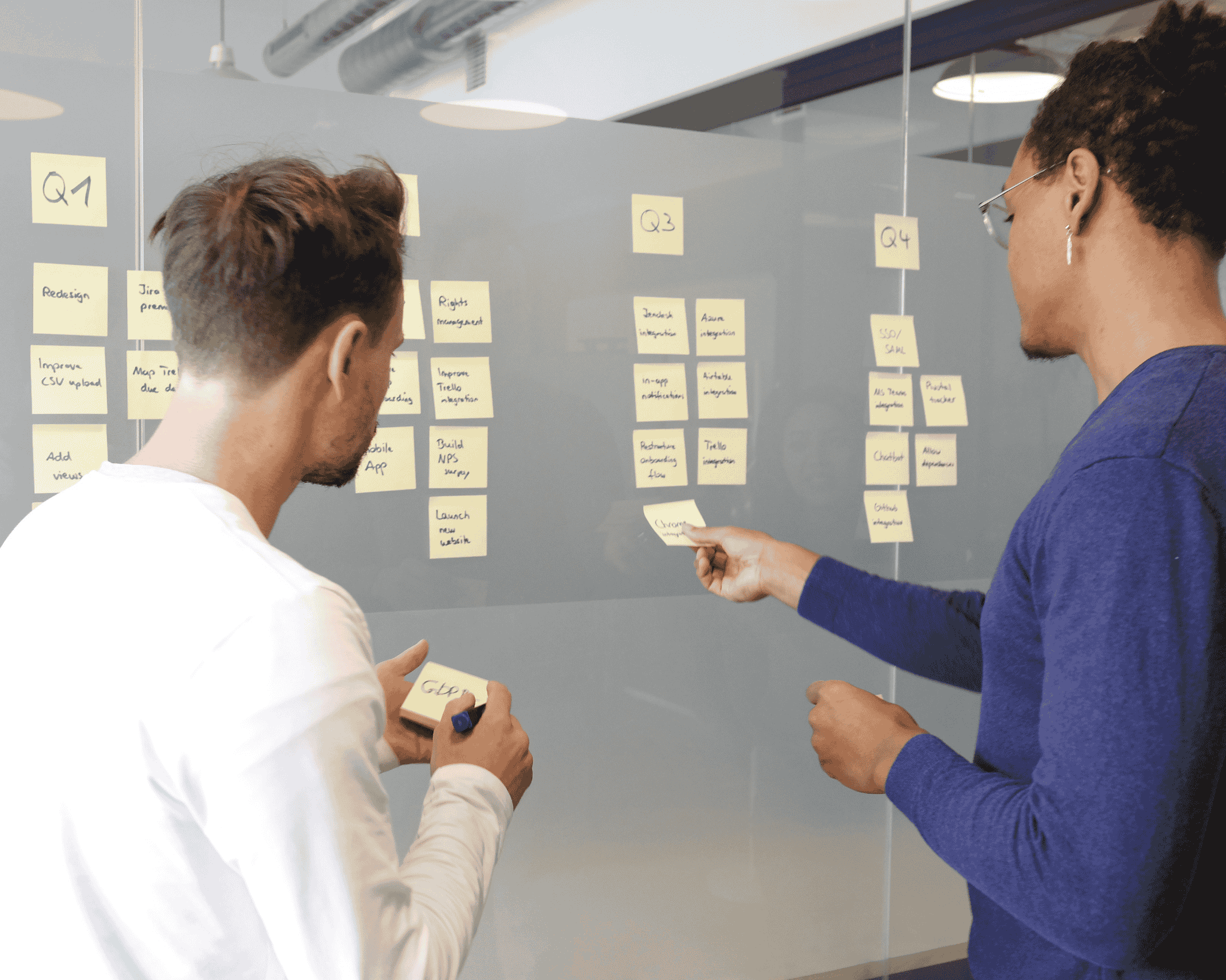 two individuals placing sticky notes on a board